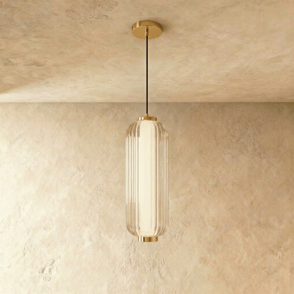 Clérachic ribbed clear glass pendant with a gold cap and ceiling plate, hanging against a warm limewash wall in the studio.
