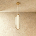 Clérachic ribbed clear glass pendant with a gold cap and ceiling plate, hanging against a warm limewash wall in the studio.