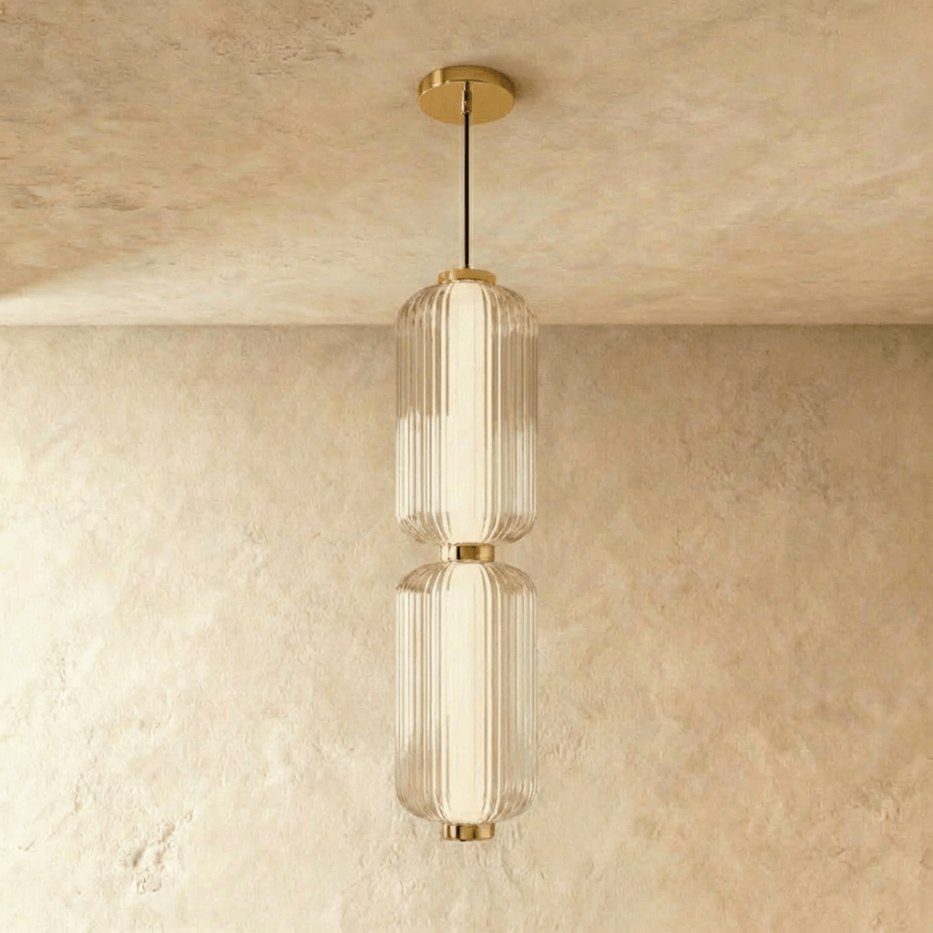 Clérachic two-tier ribbed glass pendant with gold fittings on a black cable, shown in the studio against a limewash wall.