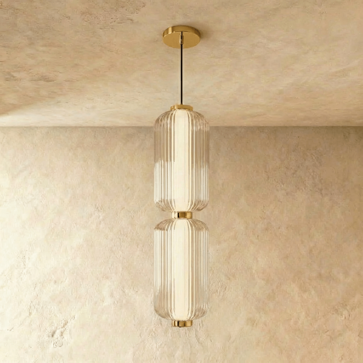 Clérachic two-tier ribbed glass pendant with gold fittings on a black cable, shown in the studio against a limewash wall.