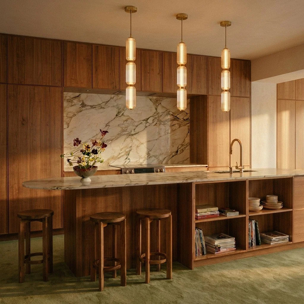 Clérachic trio of lit ribbed glass pendants glowing warm over a kitchen island with wooden stools and a marble splashback.