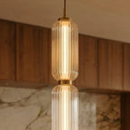 Close up of Clérachic ribbed clear glass pendant tiers with a brass-gold collar, lit warmly in a timber kitchen room.
