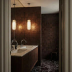 Clérachic pair of lit ribbed glass pendants with chrome caps over a marble-topped cabinet in a dark tiled room.