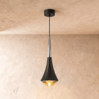 Clérachic tapered pendant light with a black body, a polished chrome neck and a warm glowing glass base, on limewash.