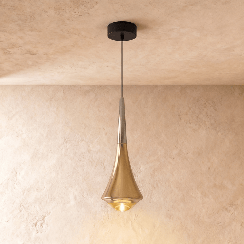 Clérachic tapered pendant in polished gold with a silver-toned neck and a glowing glass base, on a limewash wall.