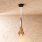 Clérachic tapered pendant in polished gold with a silver-toned neck and a glowing glass base, on a limewash wall.