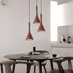 Three brick-red concrete Clérachic pendants at different heights over a round dark dining table, with a white kitchen behind.