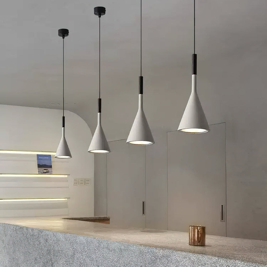 A row of four grey concrete Clérachic pendants in a curved-wall room, each with a black collar and a lit, silver-lined opening.