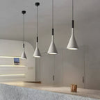 A row of four grey concrete Clérachic pendants in a curved-wall room, each with a black collar and a lit, silver-lined opening.