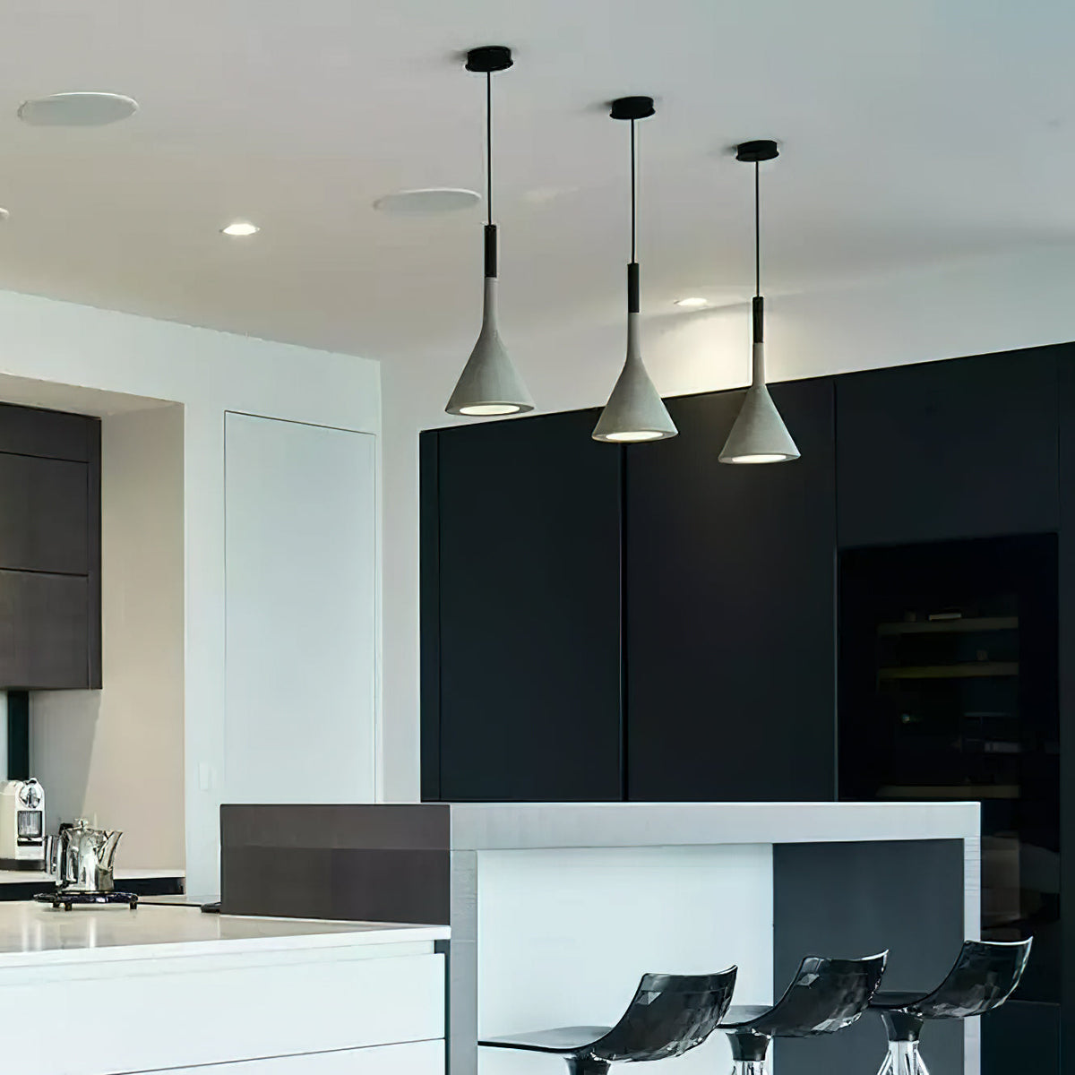 Three grey concrete Clérachic pendants over a white kitchen island with black stools, in front of dark cabinetry.