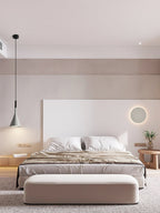 One grey Clérachic pendant hanging beside a bed with a white headboard wall, a round wall light and a pale upholstered bench.