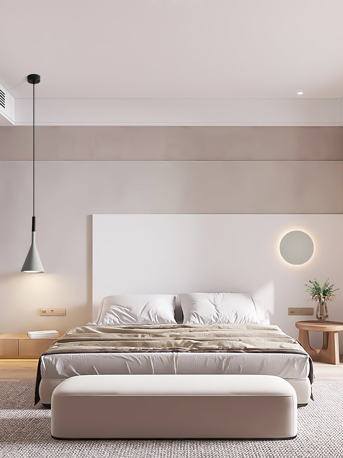 One grey Clérachic pendant hanging beside a bed with a white headboard wall, a round wall light and a pale upholstered bench.