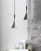 Two grey concrete Clérachic pendants against a weathered grey wall, above a white shelf with bowls and a stone sculpture.