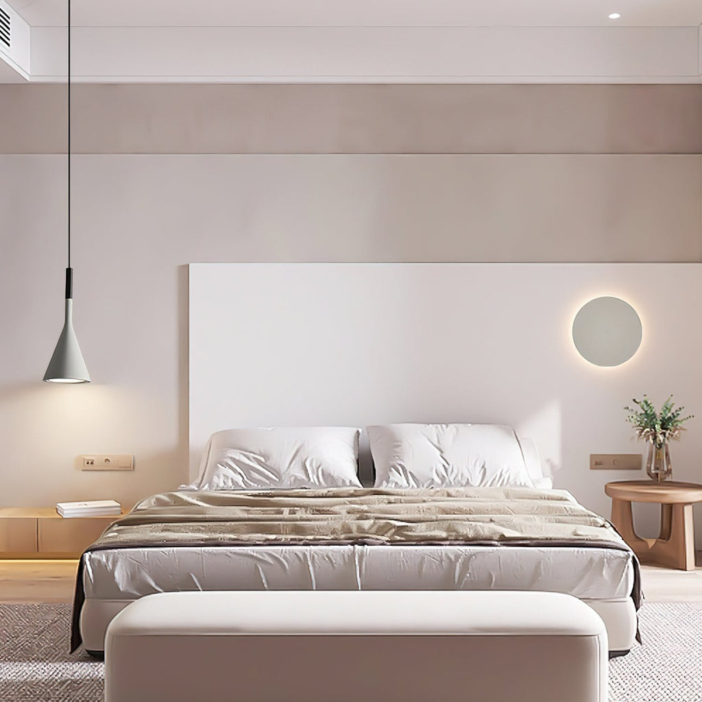 A single grey Clérachic pendant at one side of a bed with a white headboard, a round wall light and a pale bench at the foot.