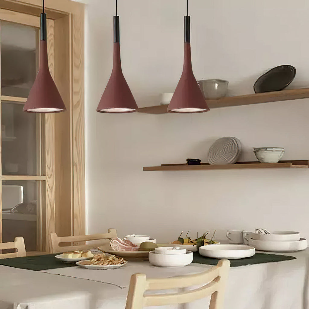 Three brick-red Clérachic pendants lit above a table laid with white plates, with wooden shelves on a pale wall behind.
