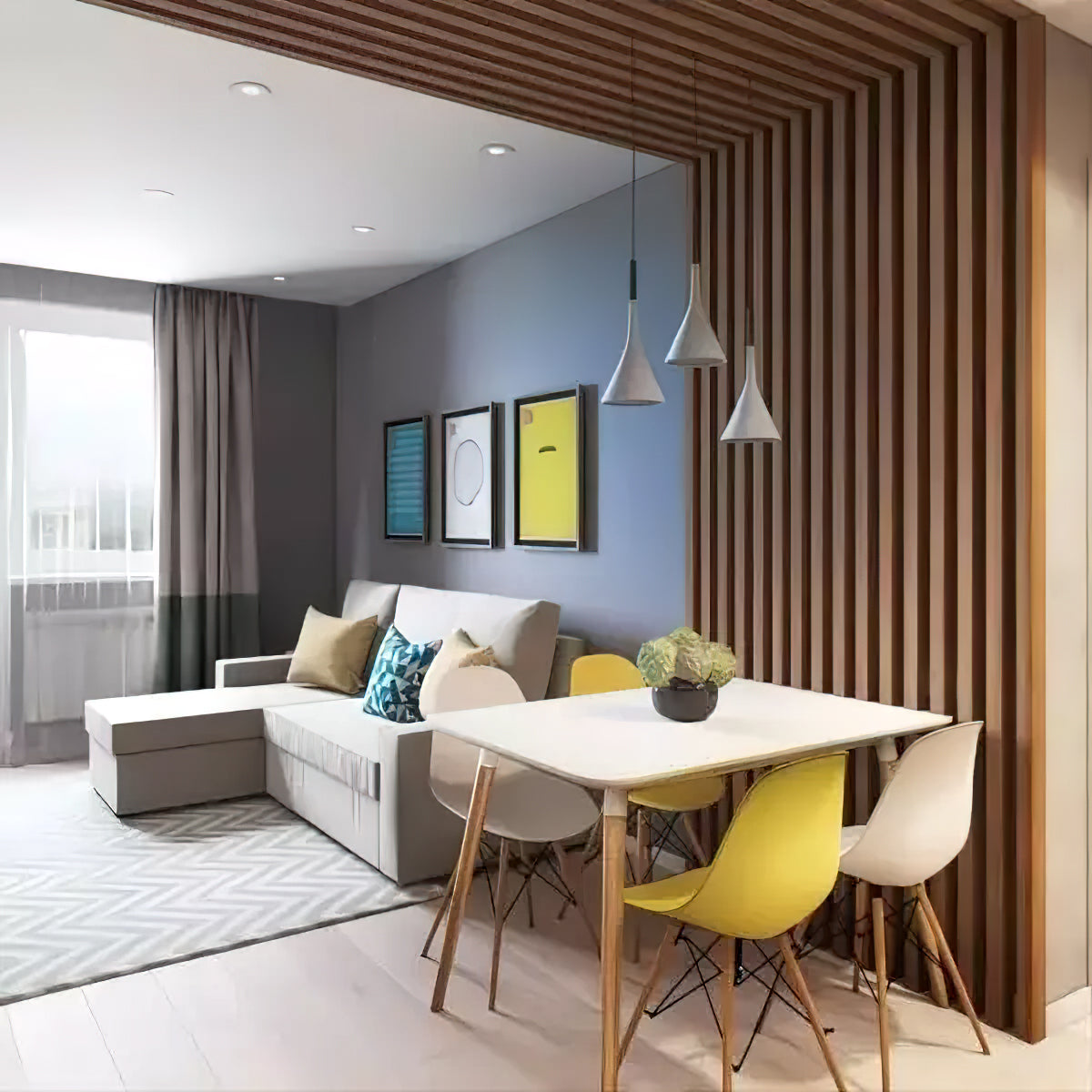 Three small grey Clérachic pendants over a white dining table with yellow chairs, in front of a slatted wood divider.