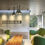 Three dark grey Clérachic pendants lit over a living area with a concrete wall, green armchairs and a wood coffee table.