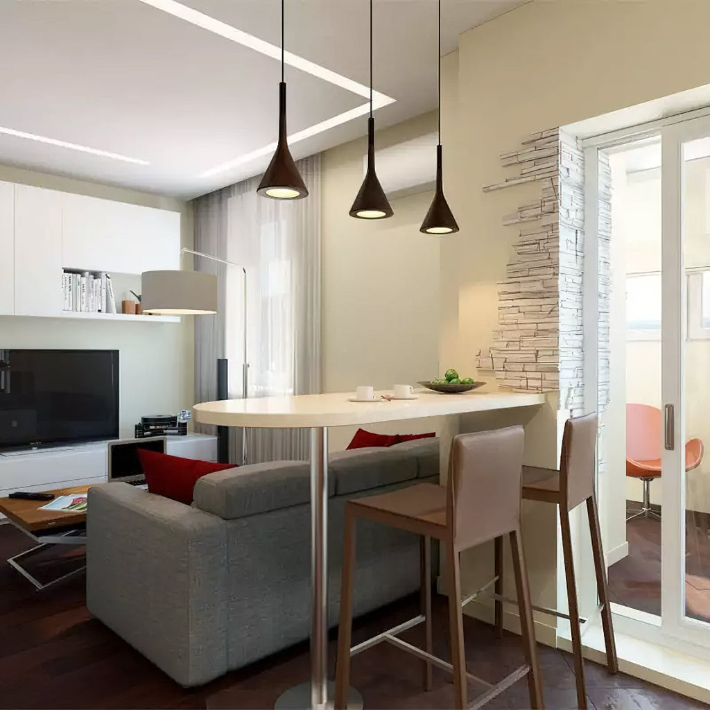 Three dark Clérachic pendants over a round-ended white table with bar stools, in a living room with a grey sofa.