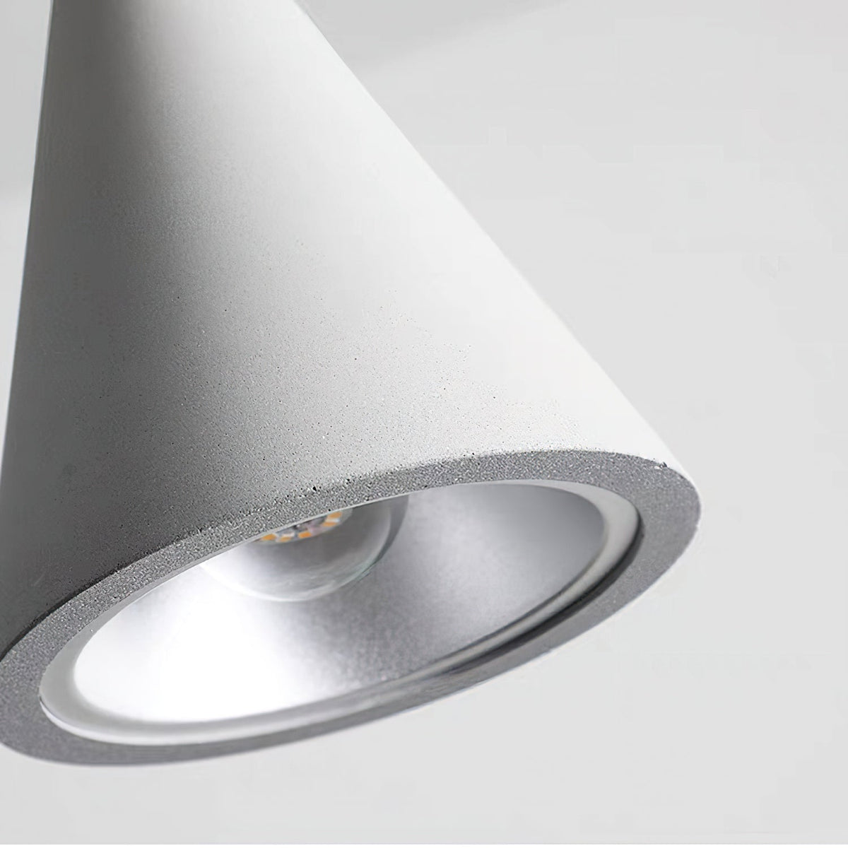 Close view of the lit inner rim and silver reflector of a light grey concrete Clérachic pendant shade.