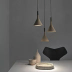 Three taupe-brown concrete Clérachic pendants over a white table with ceramics and a dark chair, against a grey wall.