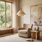 Above a cosy corner with a boucle armchair and a rough-hewn side table, a Clérachic linen pendant hangs near a tall window.