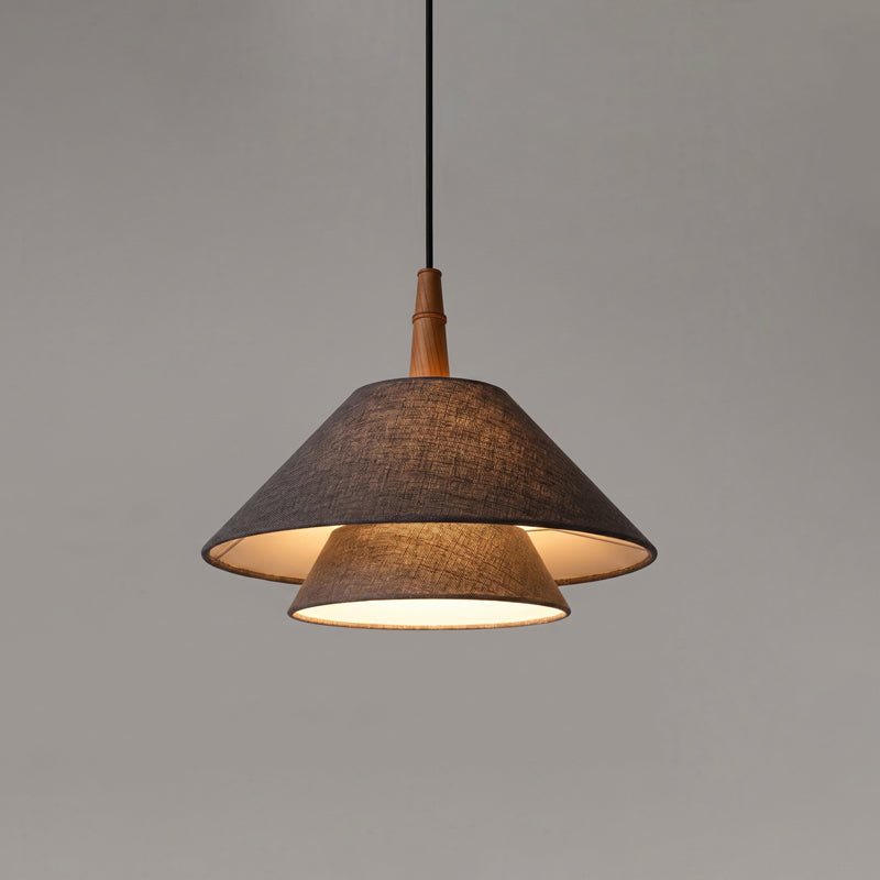A dark grey linen version of this Clérachic two-tier pendant, with a wooden neck and a black cord, against a grey wall.