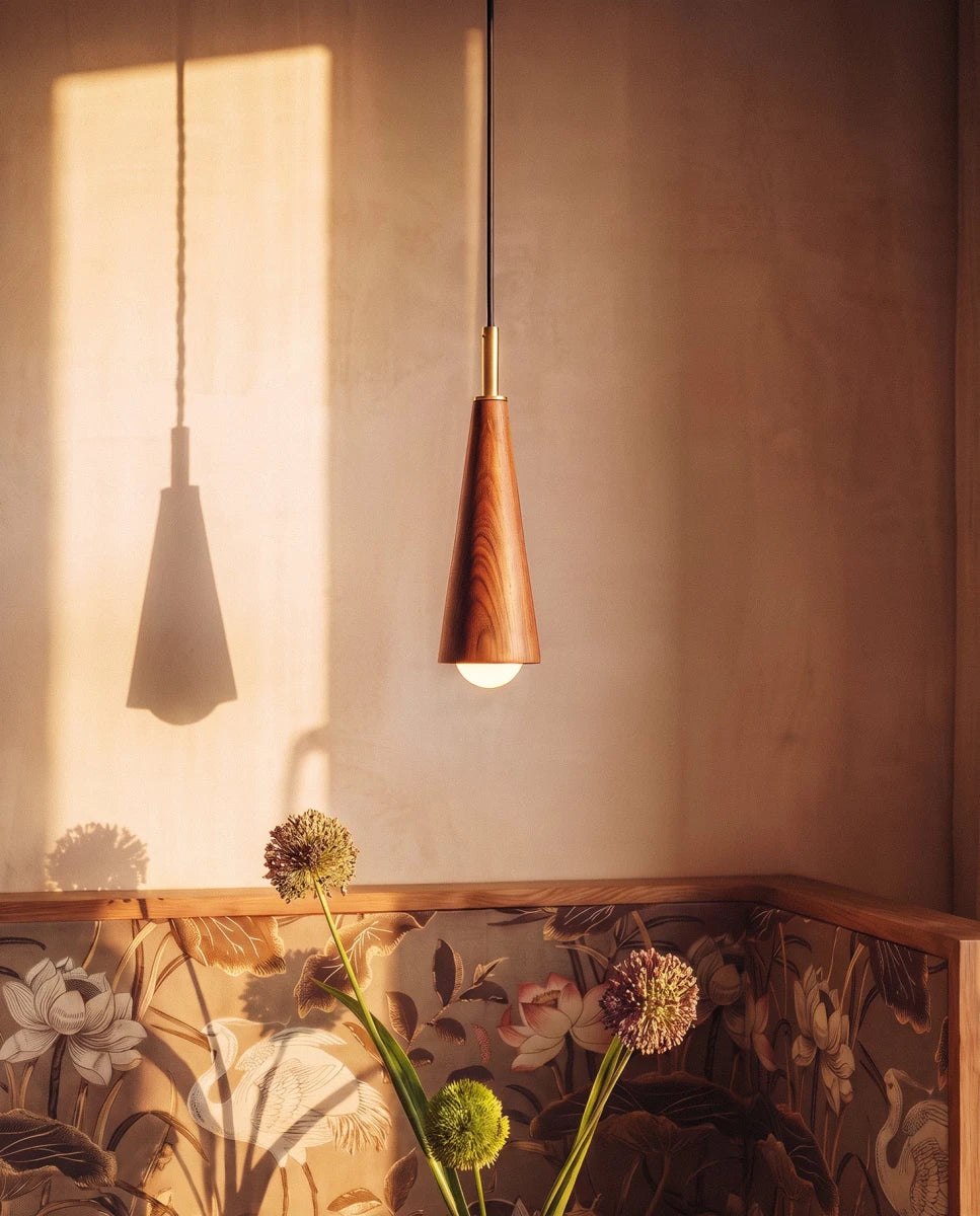 Clérachic wooden cone pendant with a brass collar and bare globe bulb, casting a long shadow beside a floral-panelled wall.