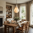 A teardrop Clérachic alabaster pendant lights a rustic dining table, with built-in shelves and a fireplace behind.