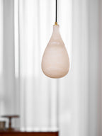 Close view of the pale, softly veined alabaster shade of this Clérachic pendant against sheer white curtains.