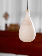 Closer view of a milky alabaster drop on a black cord with a brass collar, from Clérachic, against a blurred sideboard.