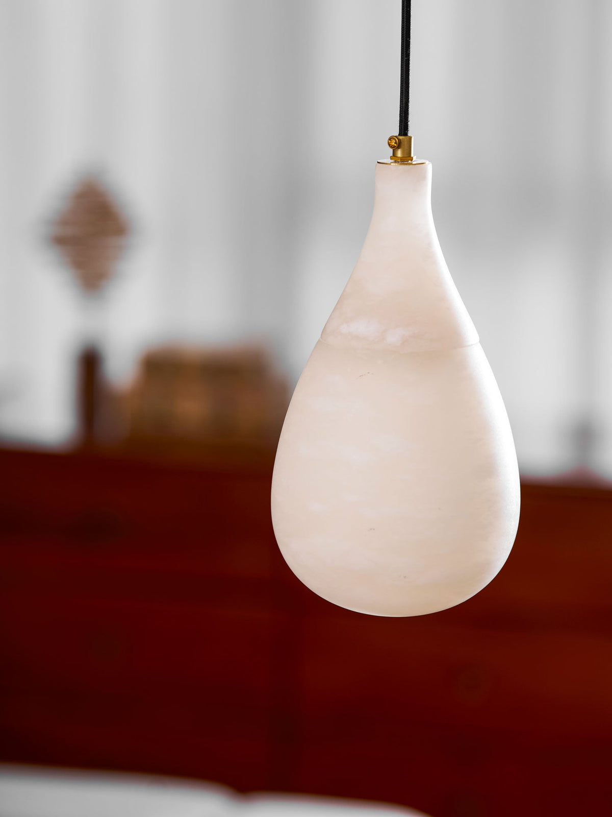 Closer view of a milky alabaster drop on a black cord with a brass collar, from Clérachic, against a blurred sideboard.
