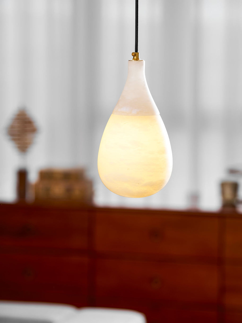 Close view of this Clérachic alabaster pendant lit, its lower half glowing amber while the neck stays pale.