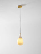 A lit Clérachic alabaster drop hangs on a long black cord from a round brass ceiling plate, against a pale wall.