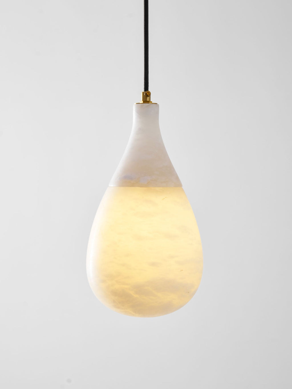 Close view of a lit Clérachic alabaster pendant on a light grey backdrop, its warm glow filling the rounded lower body.