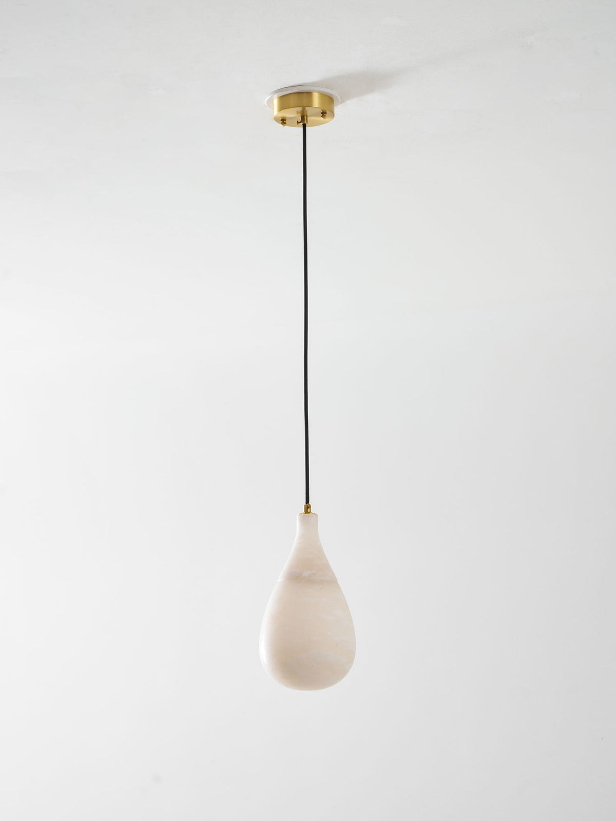 Small unlit Clérachic alabaster drop hanging from a brass ceiling plate on a thin black cord, on a pale backdrop.