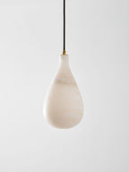 The unlit milky-white shade of this Clérachic pendant, with soft veining and a brass collar at the top.