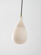 A larger, unlit Clérachic alabaster drop with pale cloudy veining, hung from a black cord with a brass collar.