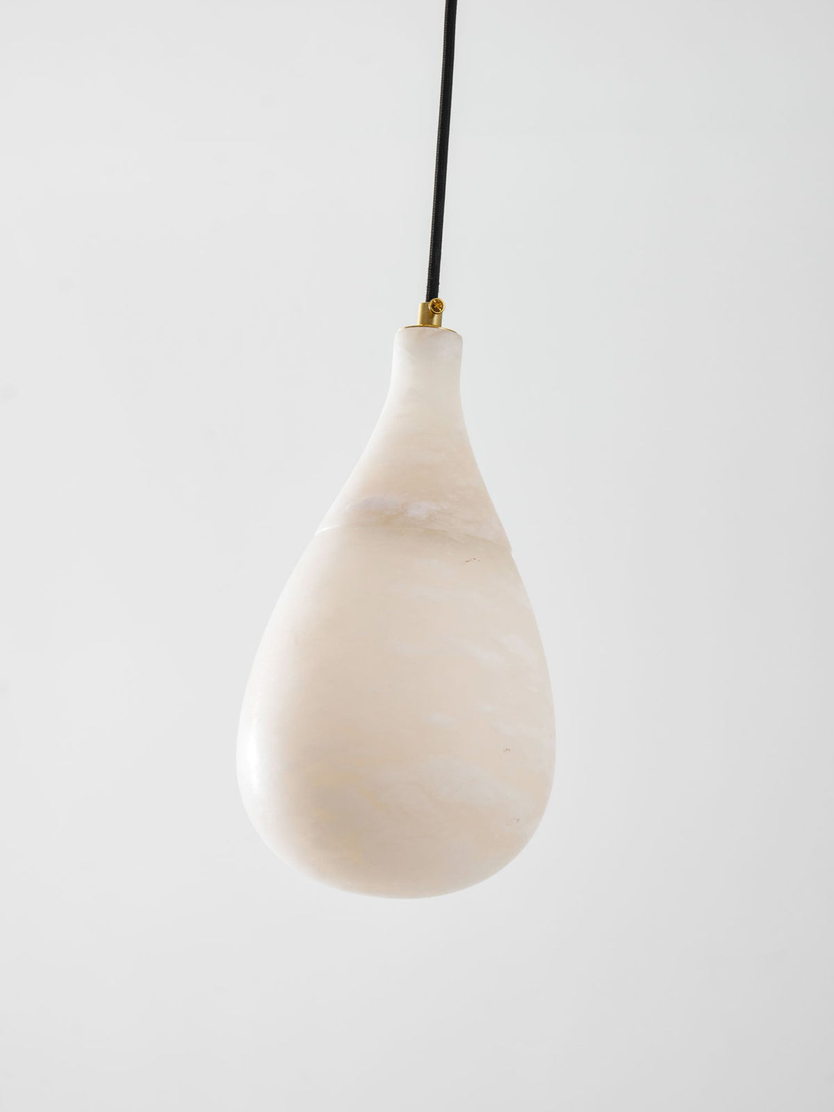 A larger, unlit Clérachic alabaster drop with pale cloudy veining, hung from a black cord with a brass collar.