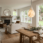 A large lit Clérachic alabaster drop hangs in an open-plan room with a stone fireplace, a sofa and a rustic dining table.