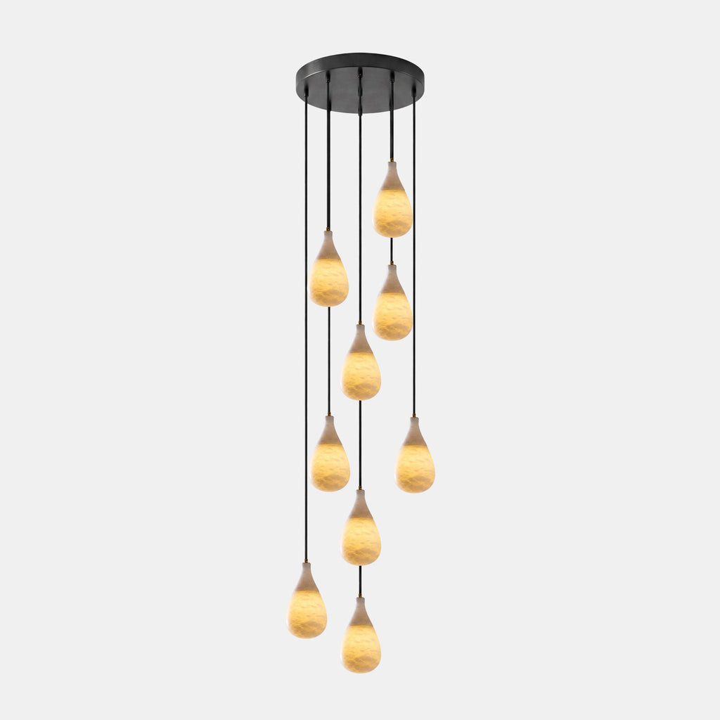 Staggered glowing alabaster drops hang from one black canopy on this Clérachic multi-head pendant, on a pale backdrop.