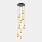 Staggered glowing alabaster drops hang from one black canopy on this Clérachic multi-head pendant, on a pale backdrop.