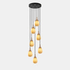Seven lit alabaster drops hang at different lengths from a round black canopy on this Clérachic pendant.