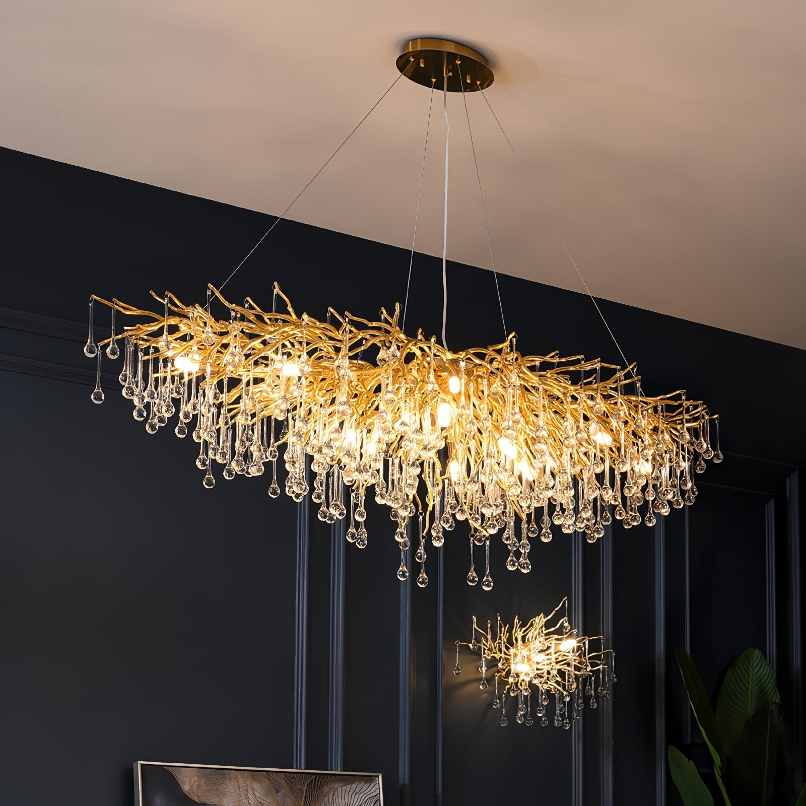 The long Clérachic teardrop chandelier lit on a navy wall, a smaller matching piece beyond.