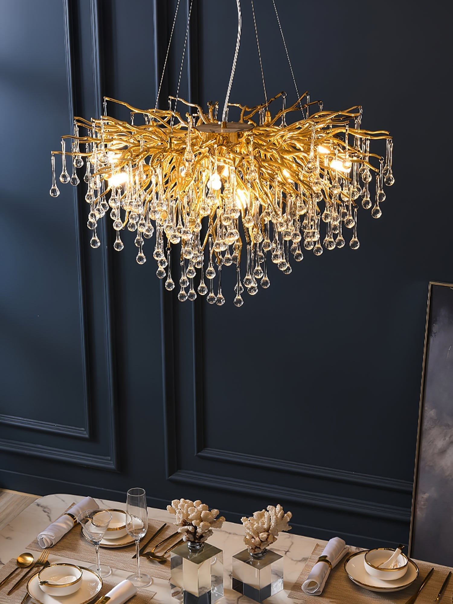 Clérachic teardrop chandelier lit low over a marble table set with coral and glassware.