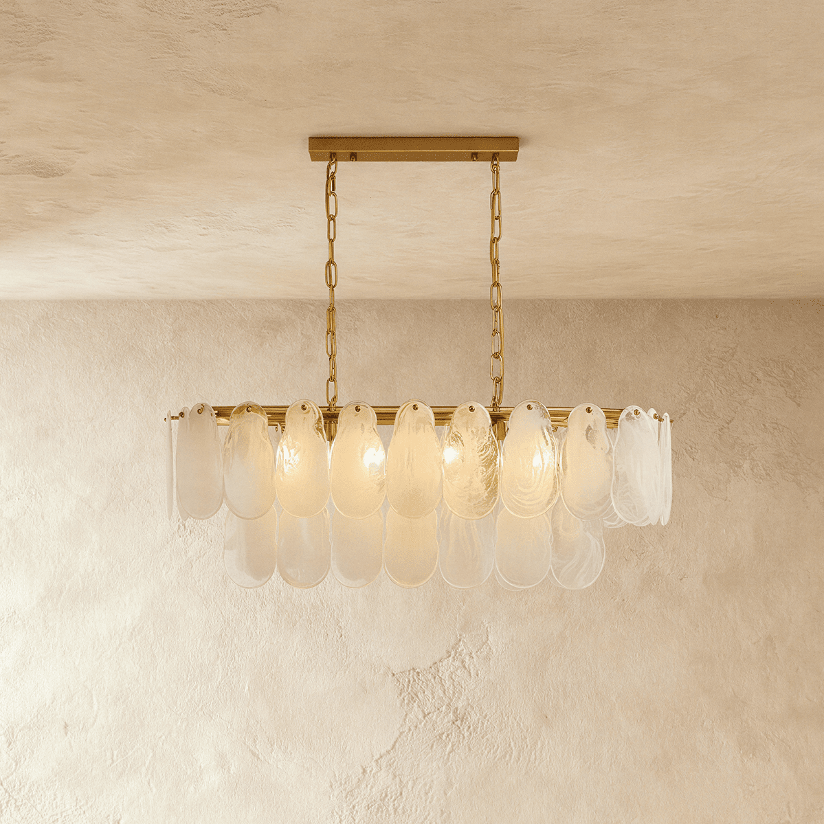 Clérachic linear chandelier with overlapping frosted glass teardrop shades on a brass bar, hung from two chains.