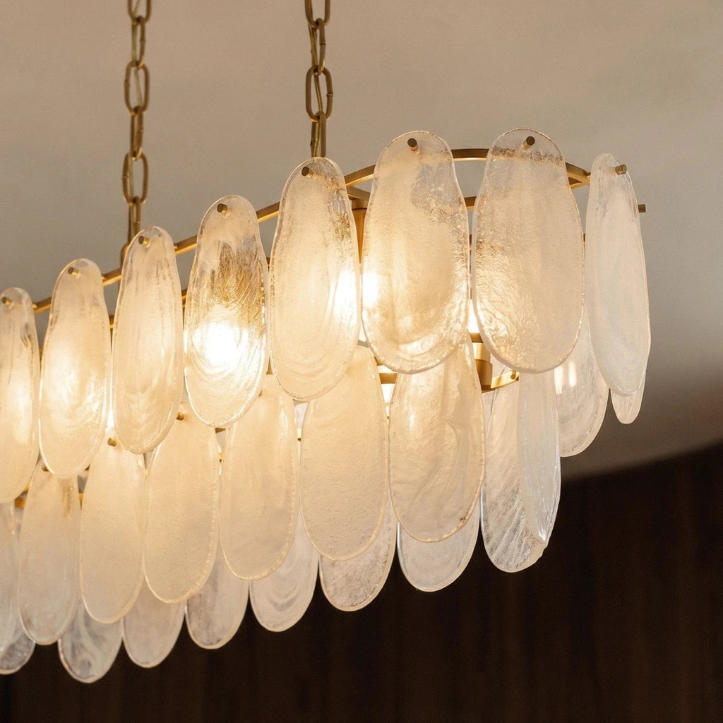 Clérachic linear chandelier close up: overlapping frosted glass teardrops lit from within on a brass frame.