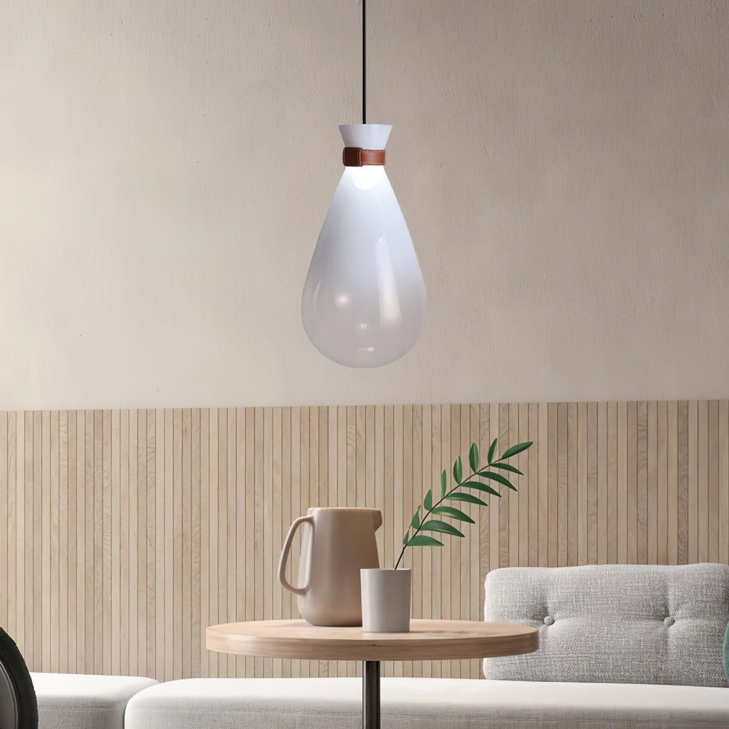 White Clérachic teardrop pendant with a leather-strapped neck, hanging over a small round wooden table with a jug and a green sprig.