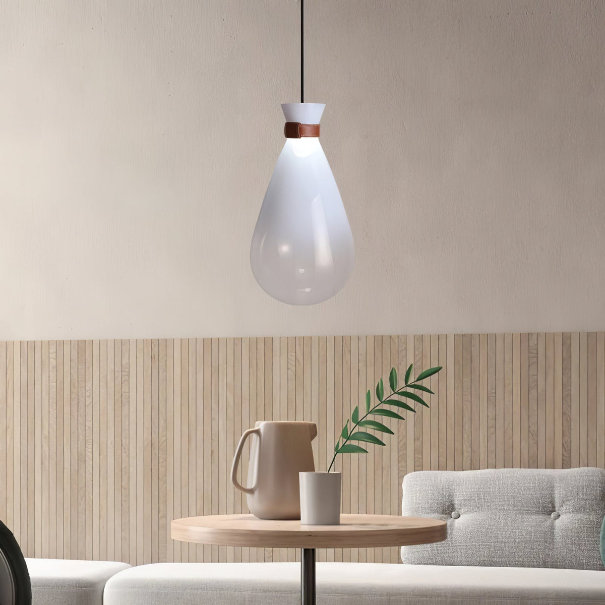 White Clérachic teardrop pendant with a leather-strapped neck, hanging over a small round wooden table with a jug and a green sprig.