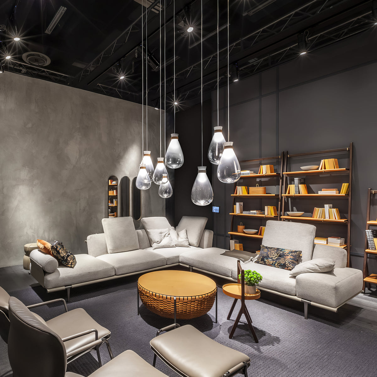 Clérachic teardrop pendants hanging at varied heights over a pale corner sofa and a round tan table, in a dark showroom.