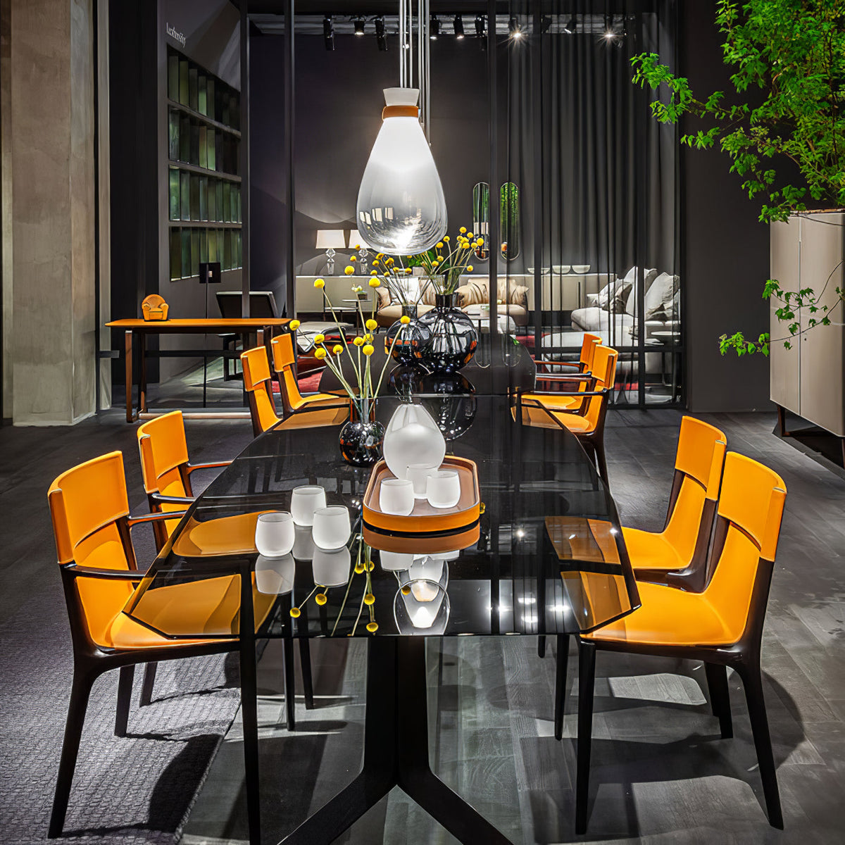 Clérachic teardrop pendant above a long dark dining table with orange chairs, in a moody room with shelves and green foliage.